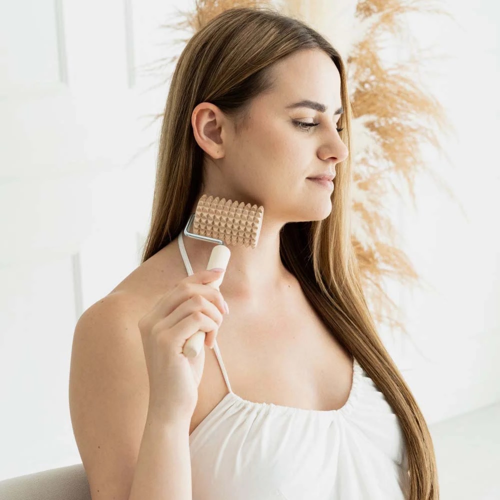 masazni_valjcek_15 - fizio trgovina woman using a beige textured neck massager roller on her neck, demonstrating a relaxing self-massage.
