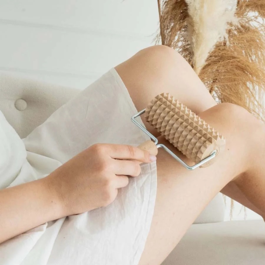 masazni_valjcek_2 - fizio trgovina person uses a beige spiked massage roller along their leg while sitting on a sofa (close-up).