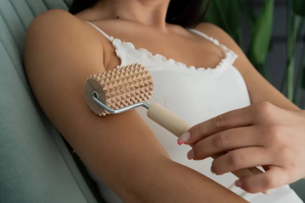 masazni_valjcek_20 - fizio trgovina person massaging their upper arm with a textured roller, a massage tool against the skin in a casual setting, wearing a white top